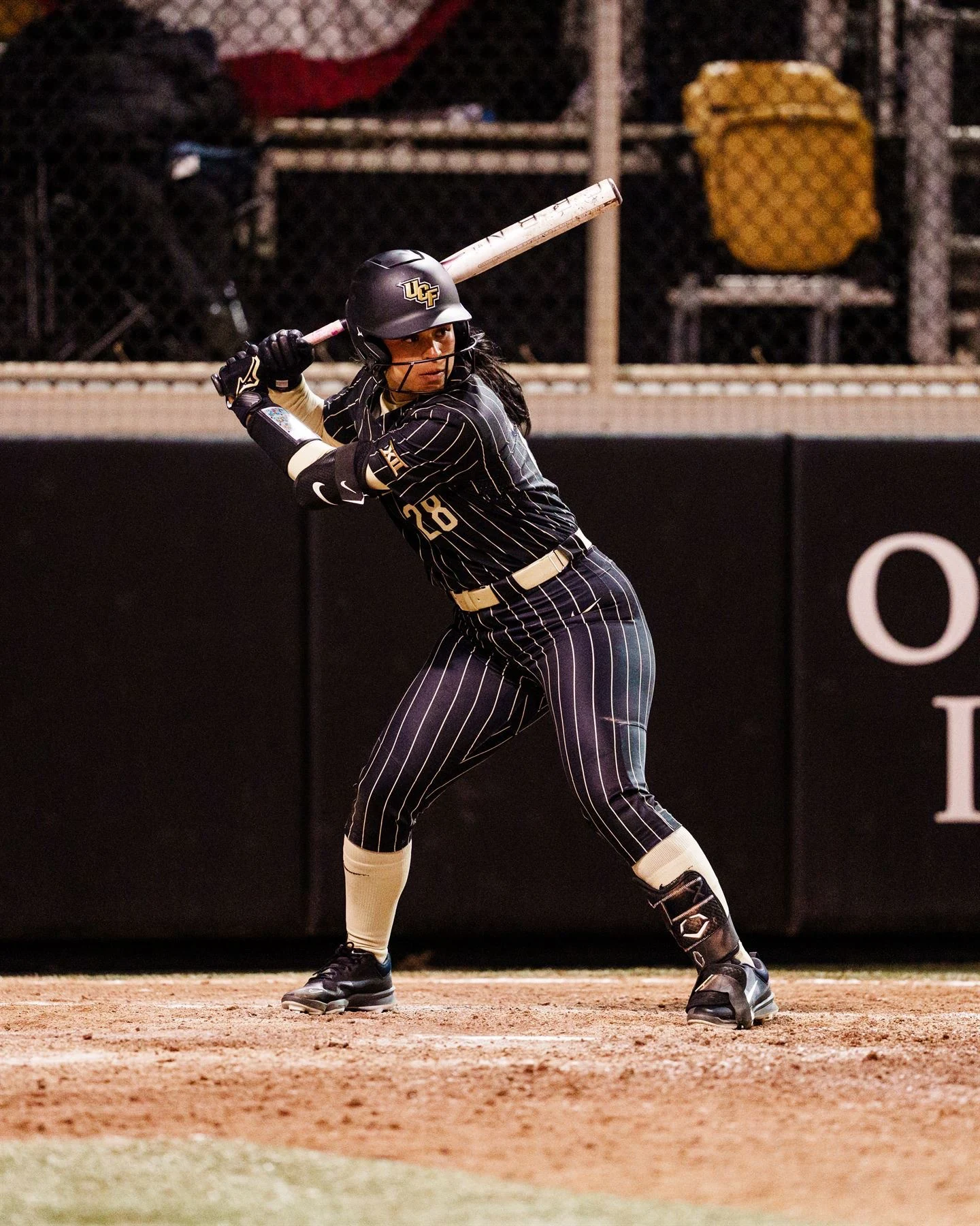Izzy Mertes in the batter's box in UCF's black pinstripe uniform, bat raised, during a night game