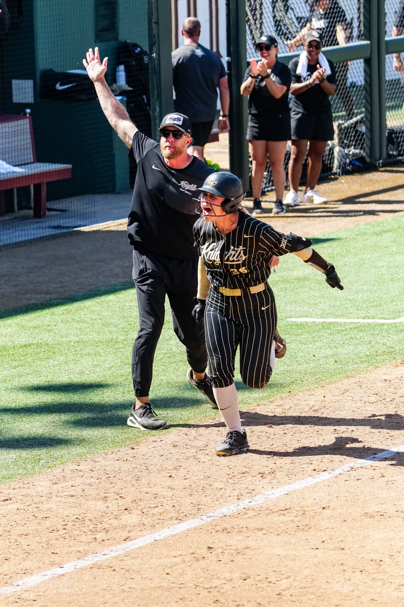Izzy Mertes rounding the bases as a UCF coach raises an arm and teammates cheer from the dugout