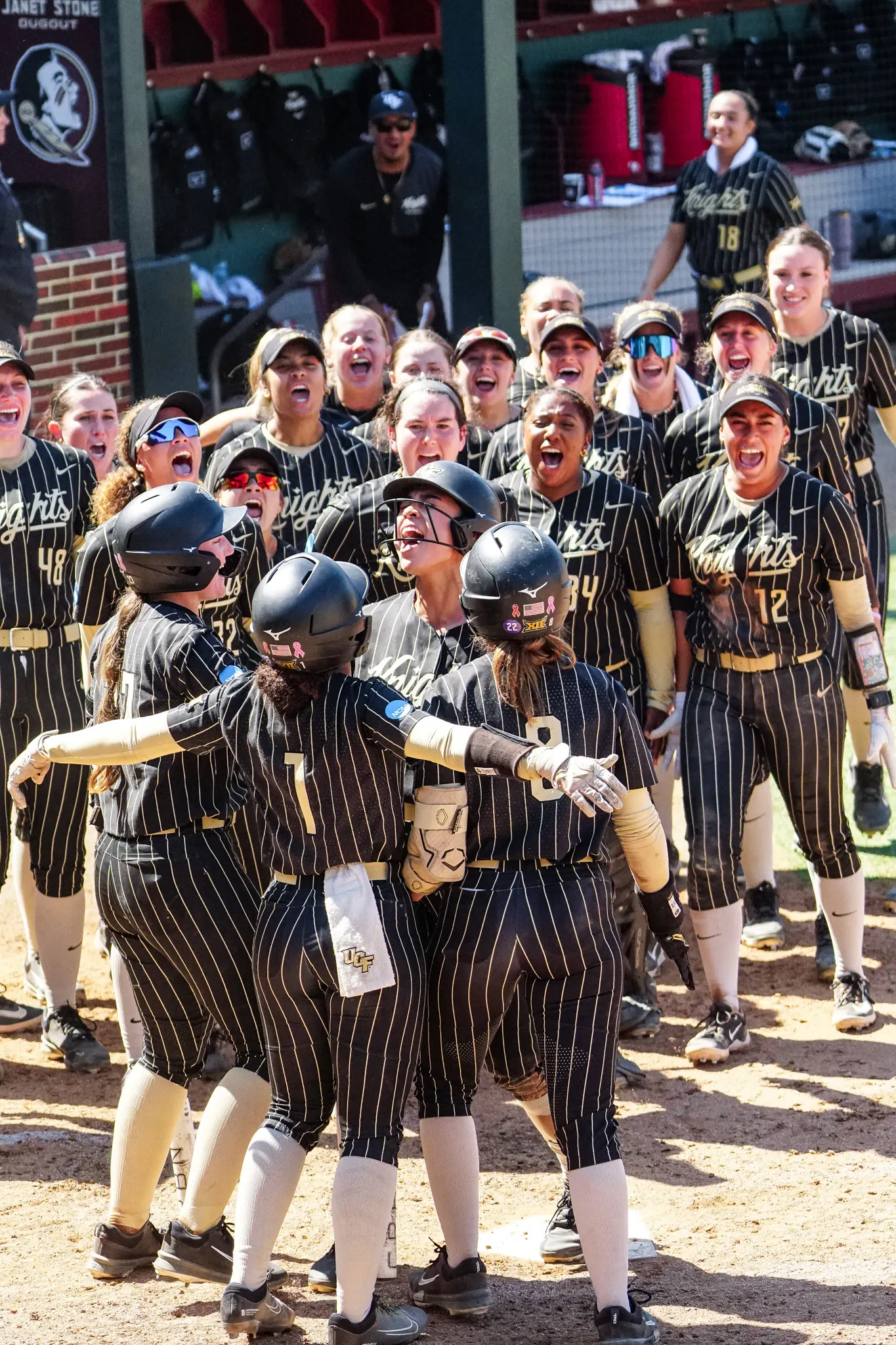 UCF teammates in black pinstripes crowding around home plate to celebrate